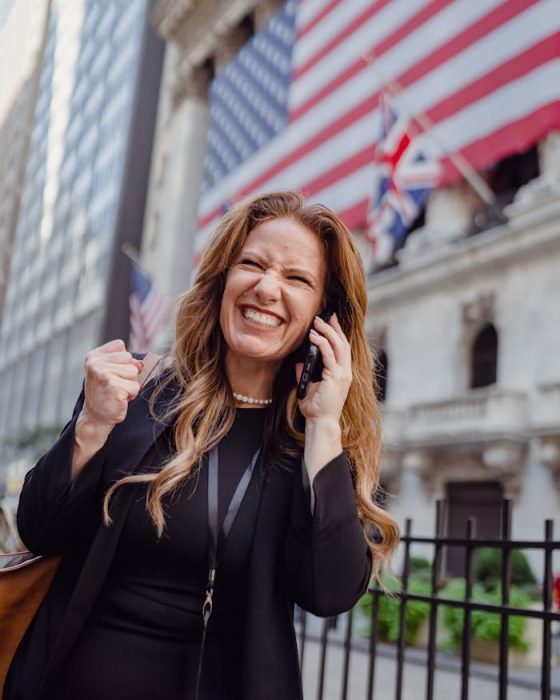 zipwp-image-13801635 Excited Woman Using Mobile Phone on a Street and US Flag in Background